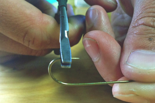 Pinching a barbed hook perpendicular to the hook.