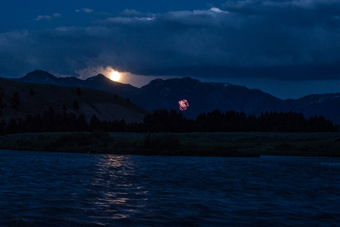 The moon peaking above the Madison Range with fireworks in the distance.